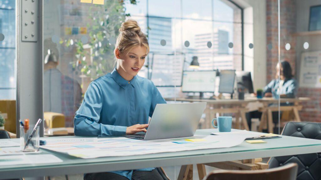 Eine Frau arbeitet an einem Laptop in einem modernen Büro, unterstützt von Shopware Kontakt für eine optimierte Kundenkommunikation.