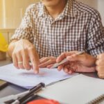 Zwei Personen sitzen an einem Tisch, wo eine Person einen Zettel unterschreibt
