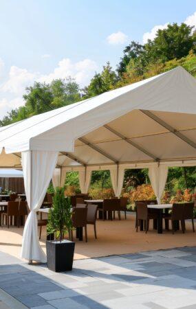 Festzelt mit weißer Plane, offener Seitenwand und Bestuhlung auf einer Terrasse bei Sonnenschein